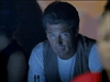 A gray-haired man in a white shirt and beige vest sits seriously in a dimly lit scene, echoing classic films like "Tall Dark and Deadly DVD (1995)," with a bottle before him and blurred figures on either side.