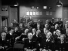 Black and white photo of men in naval and military uniforms seated attentively, with papers on the wall and an "Air Raid Shelter" sign—an authentic WWII scene from Above Us The Waves (1955) DVD.