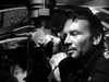 A man in a naval uniform peers through a submarine periscope in a tense scene from "Above Us The Waves (1955) DVD," set during WWII and focused on the daring mission to sink the German battleship Tirpitz.