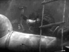Two people in dark clothing are underwater by a submarine, one with a tool, the other reaching out—a tense moment from Above Us The Waves (1955) DVD, inspired by WWII missions against the German battleship Tirpitz.