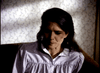 A woman with long dark hair in a light blouse sits thoughtfully on a couch in a dim, patterned room—capturing the suspenseful mood of "Murder By Reason of Insanity (1985) DVD.