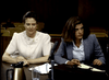 Two women sit at a table in a courtroom, one in a light pink blouse and the other in a blue blazer. Papers, water, and a coffee pot evoke scenes from rare films like the 1985 DVD Murder By Reason of Insanity.