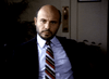 A bald, bearded man in a dark suit and light blue shirt sits indoors, staring seriously at the camera—evoking the suspenseful vibe of a psychological thriller like "Murder By Reason of Insanity (1985) DVD." The background is dimly lit and blurred.