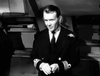 A man in naval uniform stands indoors, gesturing seriously amid black-and-white machinery, evoking the tense WWII submarine drama featured in Morning Departure (1950) DVD.