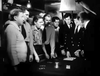A tense scene from the gripping WWII submarine drama "Morning Departure (1950) DVD" shows men in naval and civilian attire closely gathered around a table, studying cards and papers in a dimly lit room.