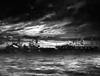 A fleet of ships is silhouetted against a dramatic, cloudy night sky, recalling scenes from the WWII submarine drama Morning Departure (1950) DVD, with shimmering lights reflected on the water.