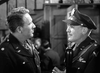 Two men in military uniforms converse indoors, both displaying U.S. Army badges and medals—just like scenes from classic films such as "A Guy Named Joe (1943)" available on DVD.