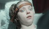 A woman with wide, fearful eyes is restrained by a leather strap under pale lighting, her shock reminiscent of scenes in rare films like The Ugly Stepsister DVD.