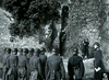 A group of uniformed soldiers stands in formation facing an ivy-covered stone wall near two people by steps—a somber scene reminiscent of classic WWII espionage drama like Decision Before Dawn (1951) DVD.