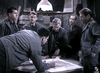 Six men in military uniforms gather around a table as one draws on a map—a tense WWII espionage drama scene, reminiscent of classic films like Decision Before Dawn (1951) DVD, set in a dimly lit, rustic wartime room.