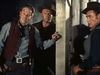 Three men in cowboy attire stand in a dim interior—a classic moment from Silver Lode (1954) DVD. The left man has a forehead wound, the center’s dark hat adds intensity to his stare, while the third man looks away.