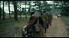 A line of soldiers in brown uniforms and helmets walks through a forest path. The lead soldier pushes a bicycle, others follow—an overcast historical scene from the World War II film April 9th (2015) DVD.