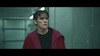 A man with wet hair in a dark shirt and red jacket stands anxiously in a dim, industrial hallway—like a moment from The House That Jack Built (2018) DVD.
