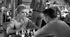 A woman in a military uniform and a man play chess across from each other in a bustling room—a scene reminiscent of classic World War II dramas like the Proud and Profane (1956) DVD.