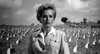 A woman in a military uniform stands somberly among white headstones under a cloudy sky—evoking scenes from the classic World War II film Proud and Profane (1956) DVD.