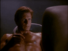 A shirtless man with short hair sits in dim light, his upper body glistening as he gazes at a blurred object—like a scene from the sci-fi horror film Dead Space (1991), now available on DVD.