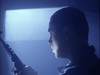 A person with a shaved head holds a rifle, facing left in dramatic lighting that shadows their face against a glowing rectangle—capturing the tense sci-fi horror vibe of Dead Space (1991) DVD.