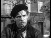 A man in a beret and scarf sits outdoors, gazing intently off-camera in this black-and-white scene from Seven Thunders (1957) DVD, evoking the tense atmosphere of a British POW film with a building and tree in the background.