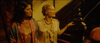 Two women in vintage attire stand by a staircase under warm lighting, evoking The Pardon (2013) DVD’s era—one wears a colorful robe, the other cream, her hand resting on the railing.