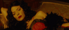 A woman with dark curls and red lipstick, draped across a vintage sofa in lace and feathers amid warm lighting, channels the mystique of Toni Jo Henry from The Pardon (2013) DVD.