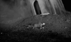 A person in a spacesuit lies face down next to a tilted, buried craft with an open hatch—evoking classic British sci-fi horror like The Quatermass Xperiment (1955) DVD—amid dirt and smoke in a dark, eerie setting.