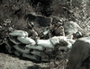 Three soldiers in helmets crouch behind sandbags in rocky terrain, echoing the tense World War II scenes found in vintage cinema like "Fighter Attack (1953)" now available on DVD.