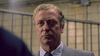 A middle-aged man in a gray suit with curly blond hair and striped tie stands indoors before bars, capturing the tense mood of a dark drama like Michael Caine in A Shock to the System (1990) DVD.