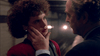 In a dimly lit scene, a person with short curly hair and red lipstick is gently touched on the cheek, their intense gaze evoking emotional moments from A Shock to the System (1990) DVD.