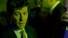A man in a suit and patterned tie stands in green-tinted light, evoking the moody vibe of "A Shock to the System (1990) DVD," with blurred figures behind him as he gazes aside like Michael Caine in the film.