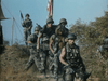 A group of soldiers in camouflage walks down a dirt path with an American flag in the background, recalling scenes from Vietnam War action dramas like "Hell on the Battleground (1988)" on DVD.