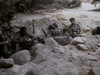 Several soldiers in camouflage uniforms rest alertly in a rocky trench, evoking gripping Vietnam War action drama scenes—like those seen in the rare "Hell on the Battleground (1988) DVD.