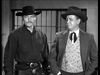 Two men in cowboy hats and Western attire stand before jail cell bars, evoking classic tension—one in a dark shirt and gun belt, the other in a suit with a bolo tie. Experience A Noose for a Gunman (1960) DVD.