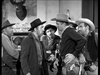 Five men in cowboy hats and western attire stand together in a saloon, deep in tense conversation—a classic scene from A Noose for a Gunman (1960) DVD. Bottles line the bar behind them, with a deer head on the wall.
