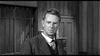 A man in a suit and tie stands before a wooden wall and barred window, looking serious—evoking classic images like the Terror in a Texas Town (1958) DVD cover.