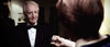 An older man in a black tuxedo smiles as someone hands him a small item in a dim room—an eerie moment echoing the supernatural terror of "Haunted Hotel (2021) DVD.