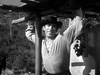 A man in a checkered shirt and wide-brimmed hat leans against a post, smiling with hills behind him—capturing the classic Western spirit of "The Ride Back (1957)" DVD.