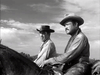 Two men in cowboy hats ride horses side by side through a rural landscape under a cloudy sky; this black-and-white image recalls classic Western drama, reminiscent of The Ride Back (1957) DVD.