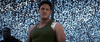 A man in a green tank top with a bandaged shoulder stands under camo netting, evoking the intense vibe of "The Tomorrow War (2021)" DVD. Blue sky filters through as another figure appears in the background.