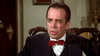 A man in a dark suit and red bow tie sits in an ornate chair, framed by classic decor and a wooden door, evoking the timeless atmosphere of a Humphrey Bogart biographical drama like "Bogie (1980)" on DVD.
