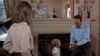 A man kneels and smiles while holding a golden trophy in front of a young boy, as a woman observes in a living room styled like the classic film "Bogie (1980)", with a fireplace and decorative mirror, as seen on DVD.