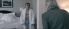 A man in a white robe and blue boxers stands in a messy hotel room with an unmade bed, facing a gray-haired person in a gray jacket—capturing the gritty atmosphere of Georgetown (2019), available on DVD.