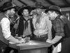 Four men in cowboy hats and western attire stand around a table in a rustic room, captured in black and white. Their serious discussion recalls the classic Western drama seen in The Westerner (1940) DVD.