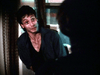 A man with wet hair and a sweaty face stands by a window, dressed in dark clothes, staring at a shadowy figure—capturing the gripping intensity found in rare films like Courage (1986) on DVD.