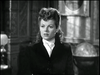 A woman with styled hair in a dark jacket and white blouse sits indoors, evoking the timeless charm of "West of the Pecos (1945)" DVD, with ornate walls and a globe behind her in a classic black-and-white setting.