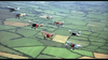 A group of vintage biplanes in colorful formation soars above patchwork fields, recalling the thrilling WWI air battles from Von Richthoften vs Brown (1971) DVD.