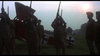 A group of soldiers in uniform stand before a red World War I biplane at sunset, rifles raised in salute—a scene recalling WWI air battles and the Von Richthoften vs Brown (1971) DVD.