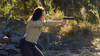 A woman dressed as a sheriff aims her handgun in sun-dappled woods, creating a tense scene worthy of horror films like the Razortooth (2006) DVD.