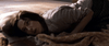 A dark-haired woman lies on her side, looking distressed, partially covered by a patterned blanket in a tense, dimly lit scene reminiscent of psychological horror films like The Night House (2020) DVD.