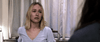 A woman with shoulder-length blonde hair and a concerned look stands indoors before light curtains, evoking a scene from The Night House (2020) DVD, as she gazes at someone partially visible in the foreground.
