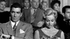A serious man in a suit sits beside a smiling blonde woman in pearls, evoking classic movie scenes—like those in "The Rise and Fall of Legs Diamond (1960)" DVD—with an audience visible behind them.